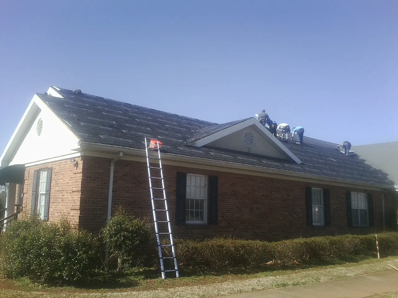 Crew tearing shingles off a brick ranch roof with a ladder set — Metal Roof Repair work by our crew in Arvonia