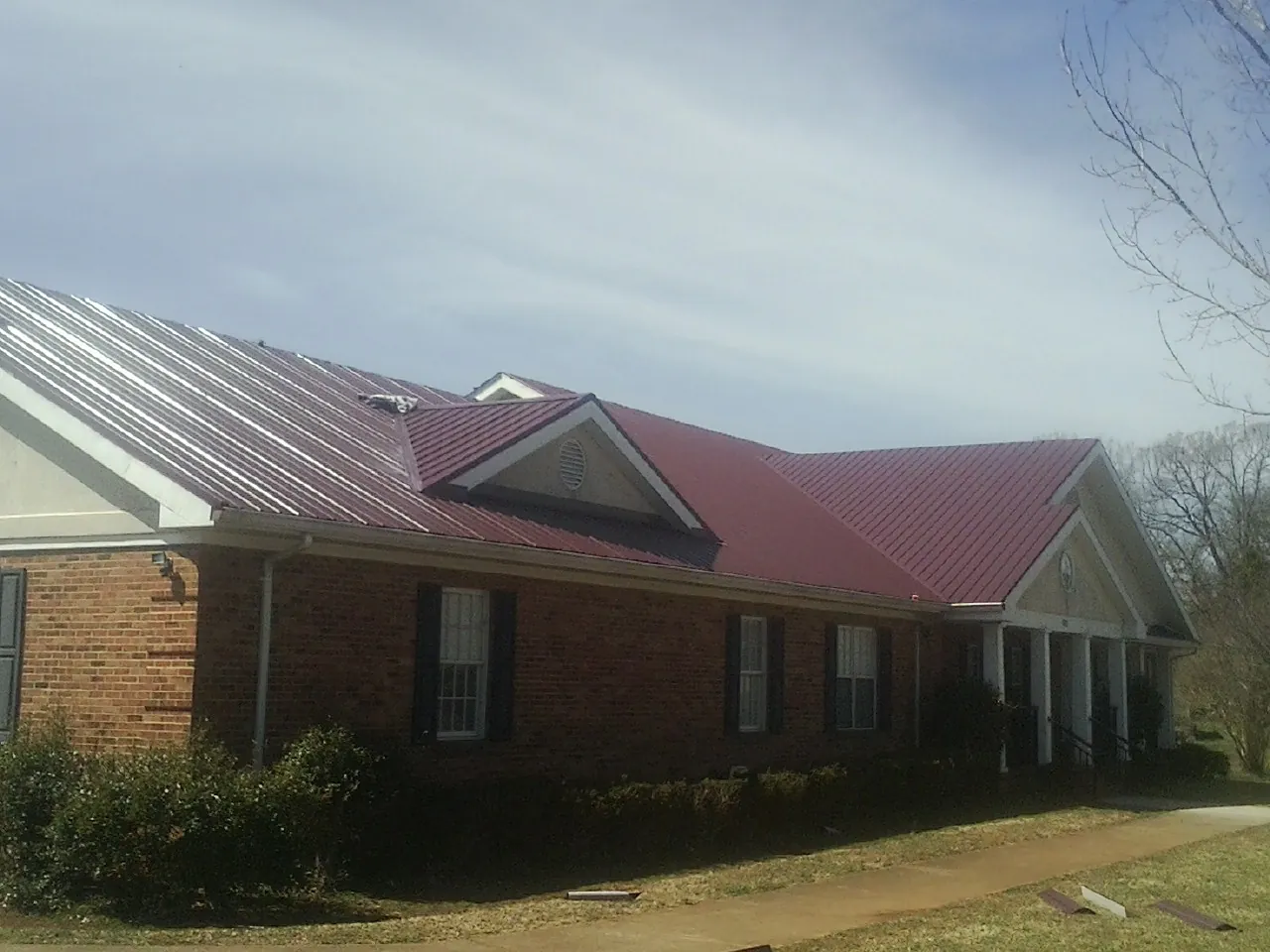 Red metal roof with gabled entries on a long brick building, from a Hail Damage Roof Repair job in Arvonia