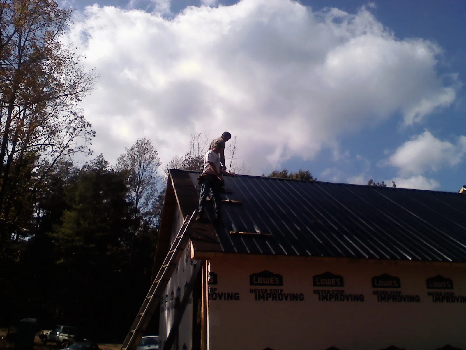 Roofer fastening dark metal panels high against a cloudy sky, from a Roof Inspection job in Arvonia