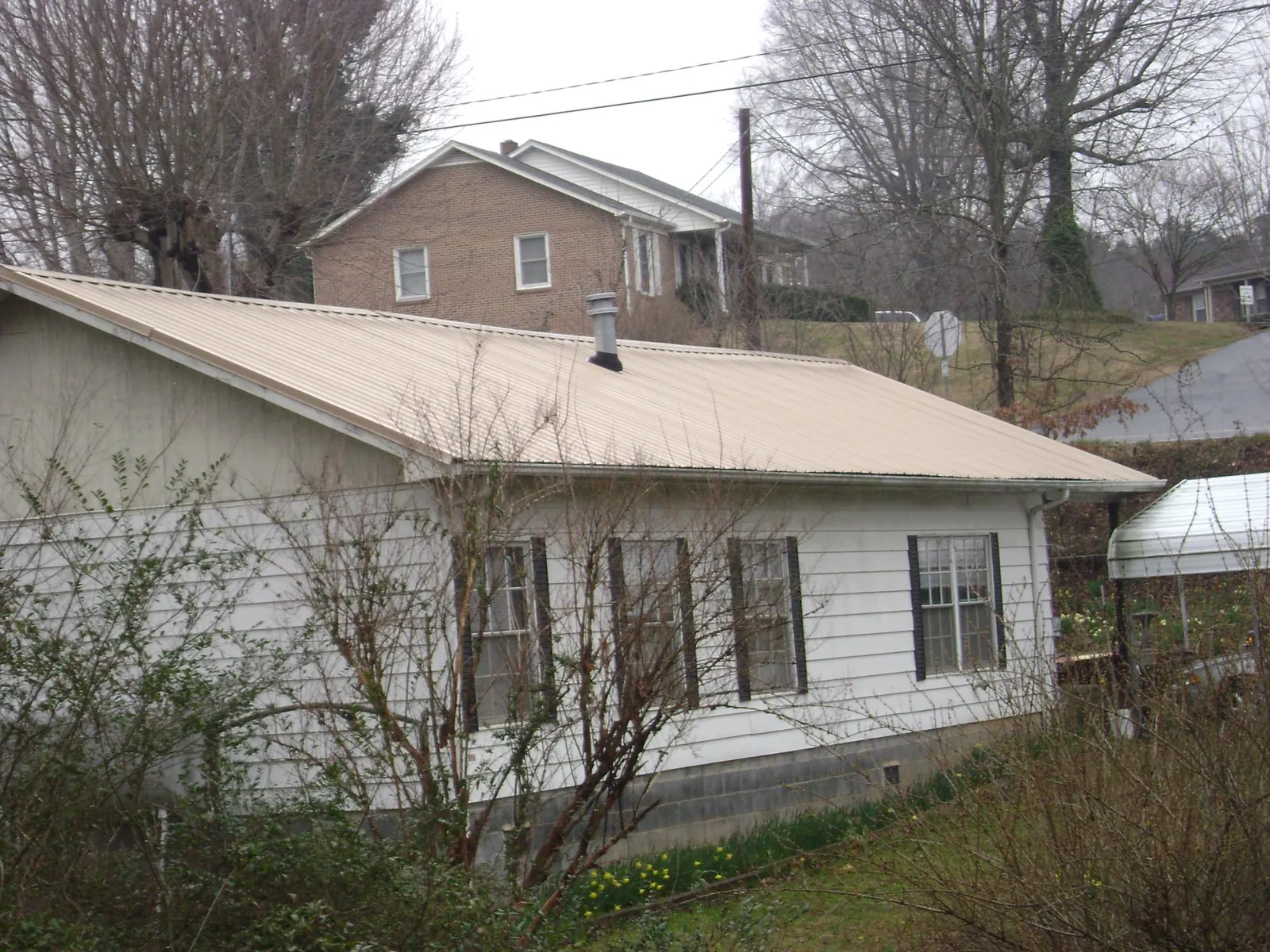 Tan metal roof on a white sided house set into a hillside — Commercial Roofing by Roofing Brothers in Arvonia