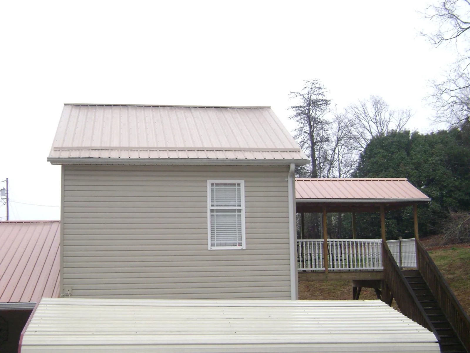 Tan metal roofs on a two story addition and attached porch, from a Roof Replacement job in Arvonia